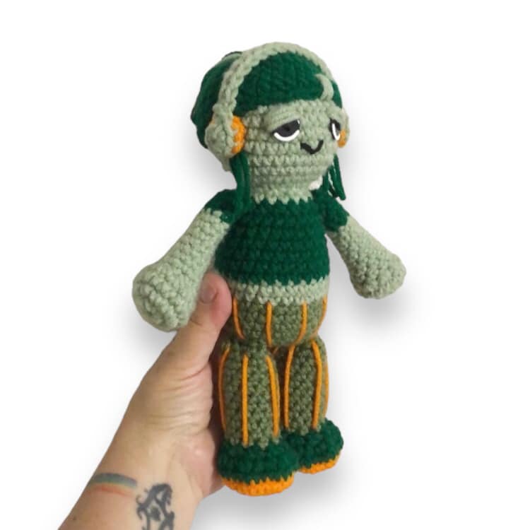 A crochet doll resembling Carmella Creeper being held up against a white background. 