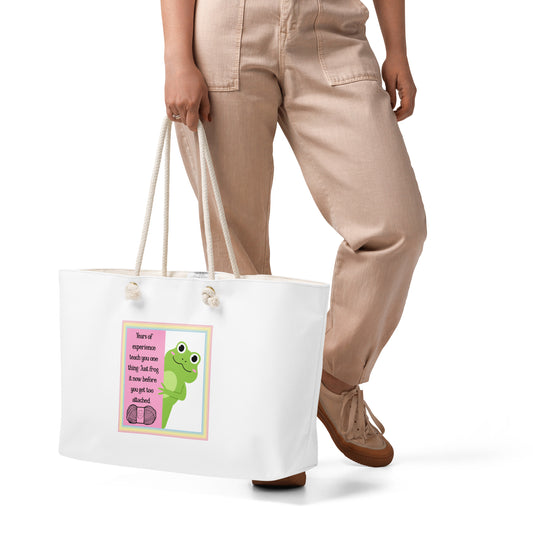 A white tote bag with a frog peering around a pink wall inside a rainbow border. 