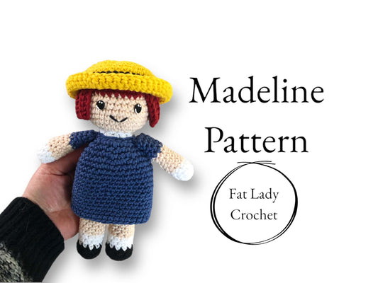 A crocheted doll resembling Madeline from the series Madeline being held up against a white background, with text that reads "Madeline Pattern," and "Fat Lady Crochet." 