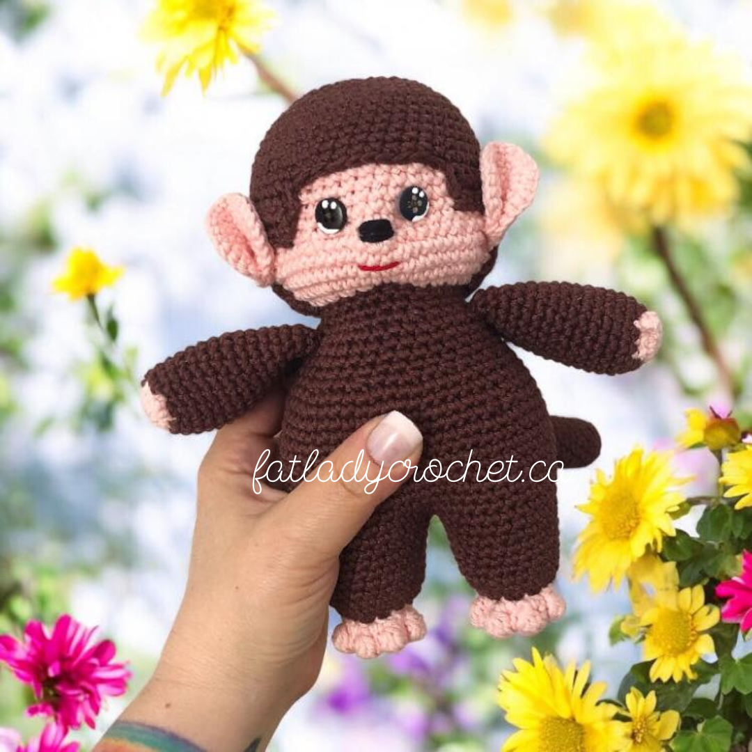 Hand holding a crochet monchhichi doll against a flower background. 