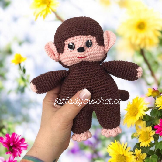 Hand holding a crochet monchhichi doll against a flower background. 