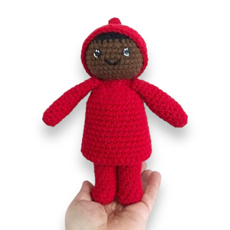 A crocheted doll resembling Peter from the Snowy Day by Ezra Jack Keats being held up against a white background. 