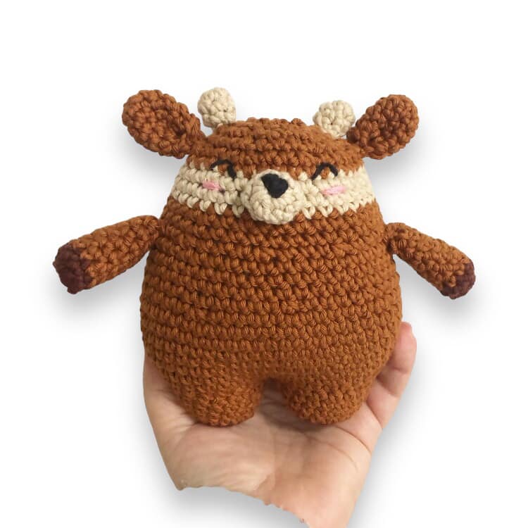 A crocheted doll resembling a deer being held up against a white background. 