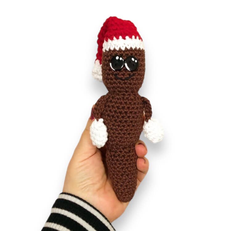 A crochet doll resembling Mr. Hanky the Christmas Pattern being held up against a while background.