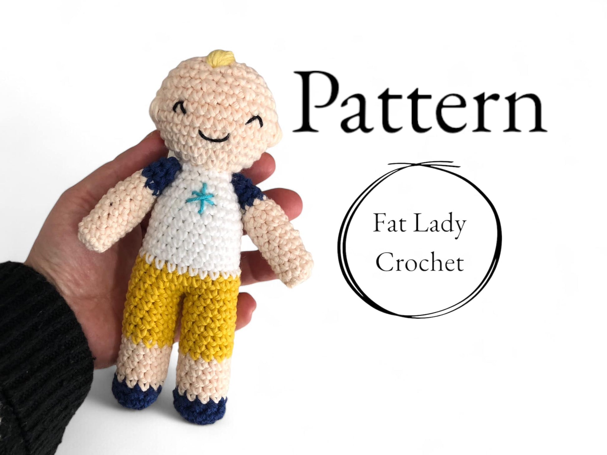 A crocheted doll pattern called 'JJ' being held in a person's hand. The doll has a smiling face, wearing a white and denim outfit with yellow shorts. 