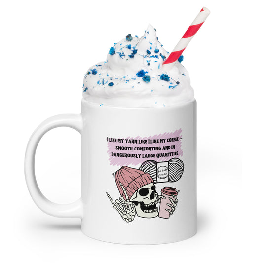 White mug with skeleton in a dark pink beanie holding a cup of coffee and making the rock on hand sign. 