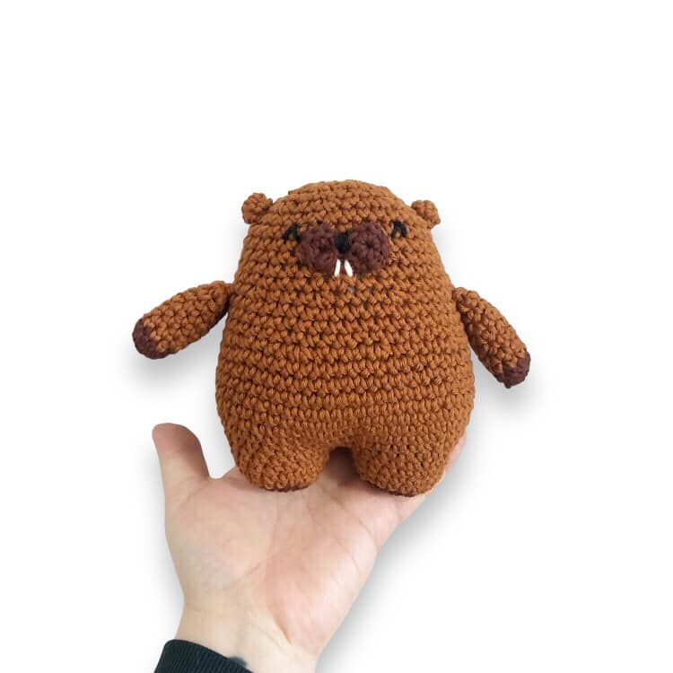 A crochet beaver plushie being held up against a white background. 