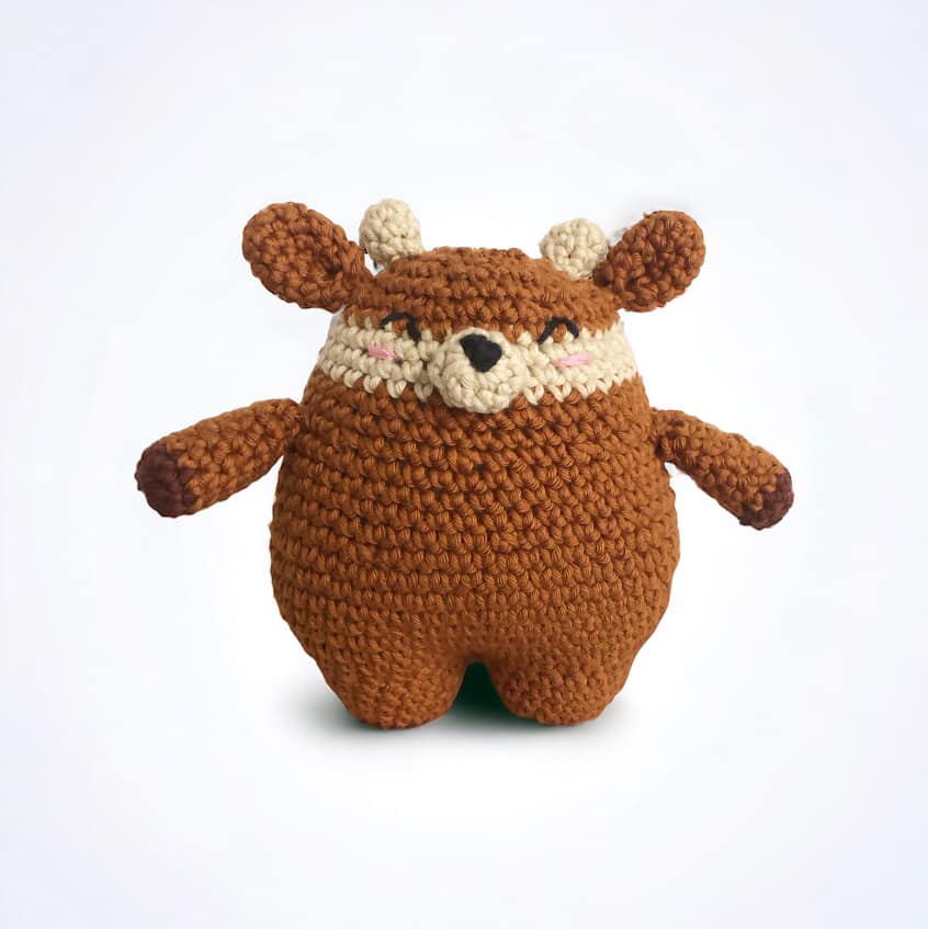 A crocheted doll resembling a deer standing against a white background. 