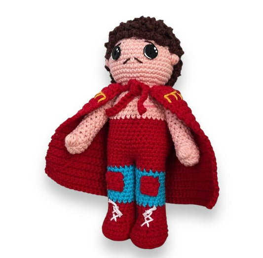 Crocheted doll of Ignacio from Nacho Libre with cape and boots against a white background. 