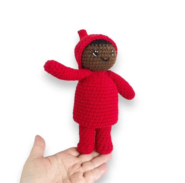 A crocheted doll resembling Peter from the Snowy Day by Ezra Jack Keats being held up against a white backround. 