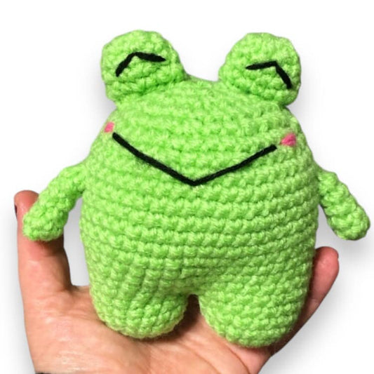A crocheted doll resembling a green toad being held in a person's hand. 