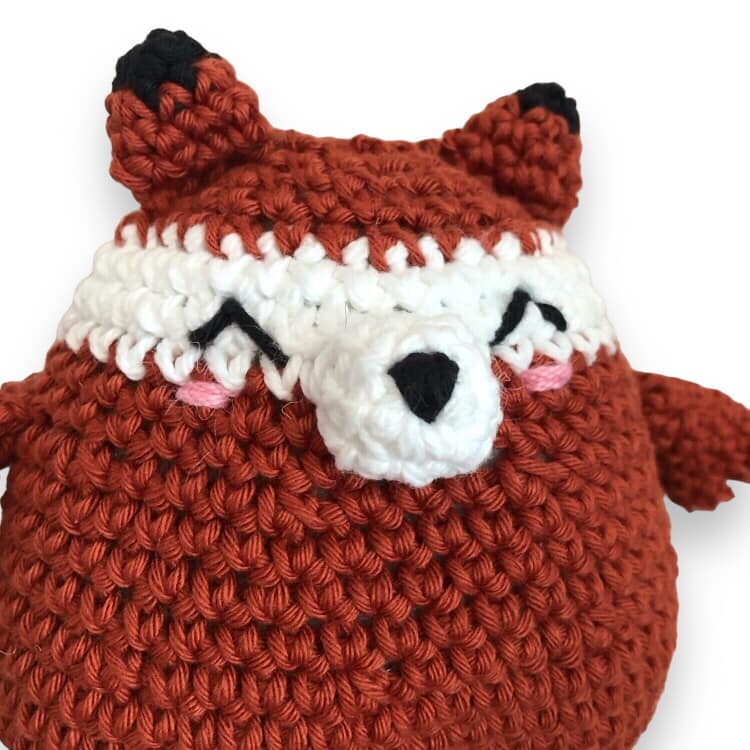 A crochet doll resembling a chubby fox against a white backgrounds. 