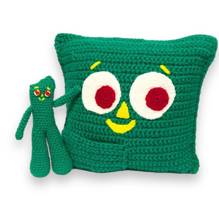 A crocheted pillow and doll of the cartoon character Gumby standing against a white background. 