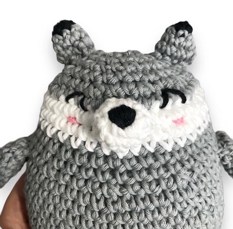 A close up of a crocheted wolf plushie against a white background. 