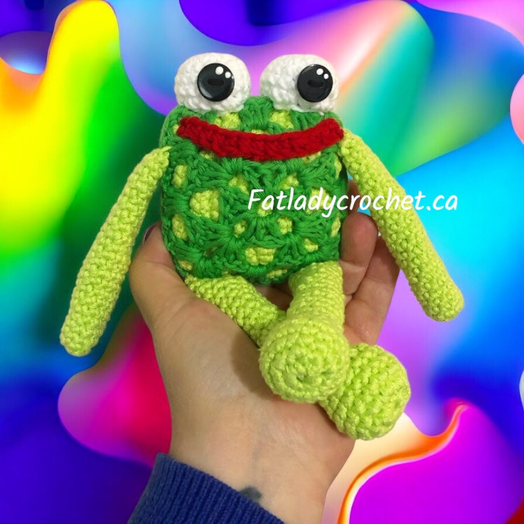 Crocheted frog toy held in a hand with a colorful, abstract background and 'Fatladycrochet.ca' branding.