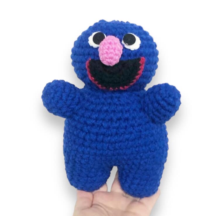 A crocheted doll of rover from Sesame Street being held up against a white background. 