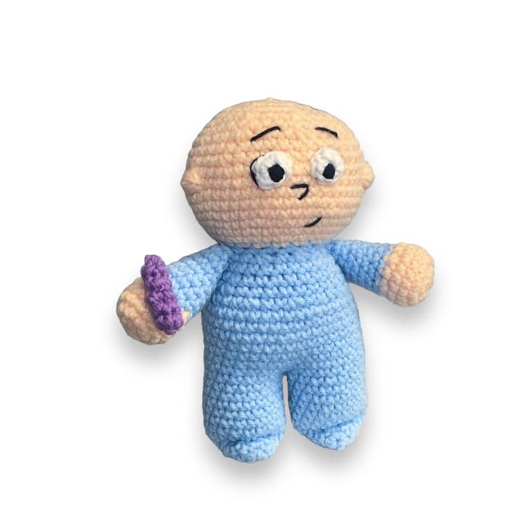 A crocheted doll resembling Harold from Harold and the Purple Crayon being standing against a white background. 