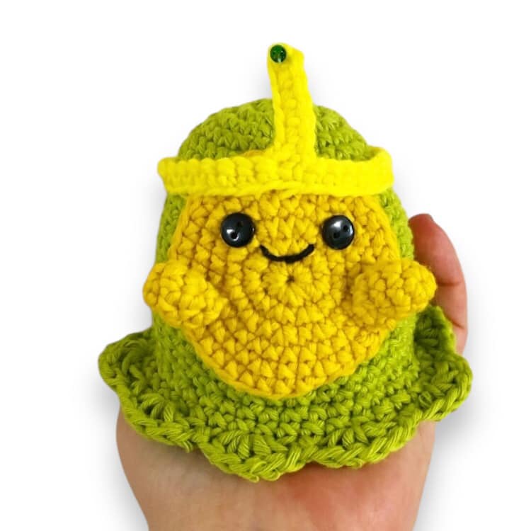 A crochet version of Slime Princess from Adventure Time being held up against a white background. 