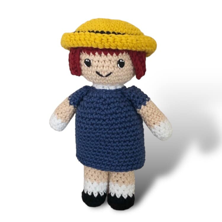 A crochet doll resembling Madeline from the series Madeline standing against a white background. 