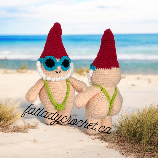 A crochet gnome doll dressed in a green mankini standing on a beach backdrop with a "Fatladycrochet.ca" watermark. 