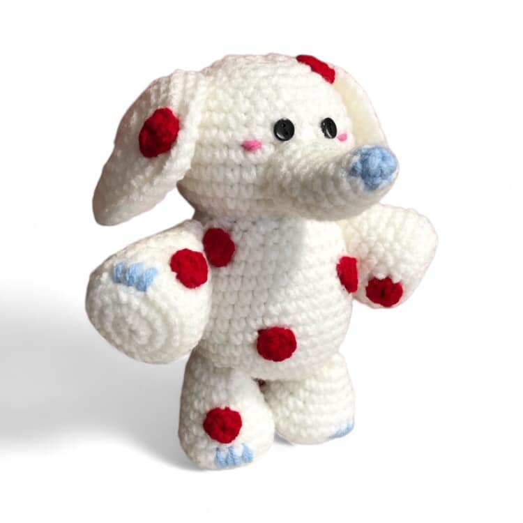 A white and red spotted crochet elephant from Rudolph the Red Nosed Reindeer standing against a white background. 