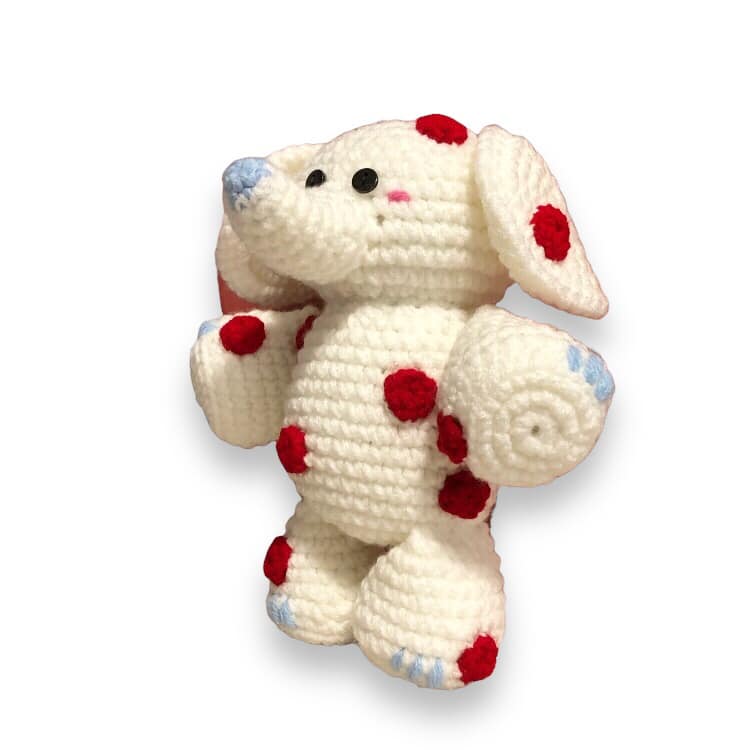 A white and red spotted crochet elephant from Rudolph the Red Nosed Reindeer standing against a white background. 